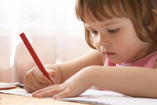 A little girl is writing with a red pencil.